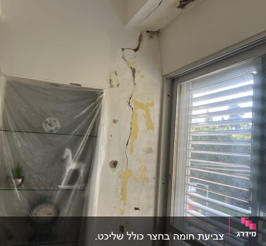 קיר עם סדקים וכתמי רטיבות ליד חלון